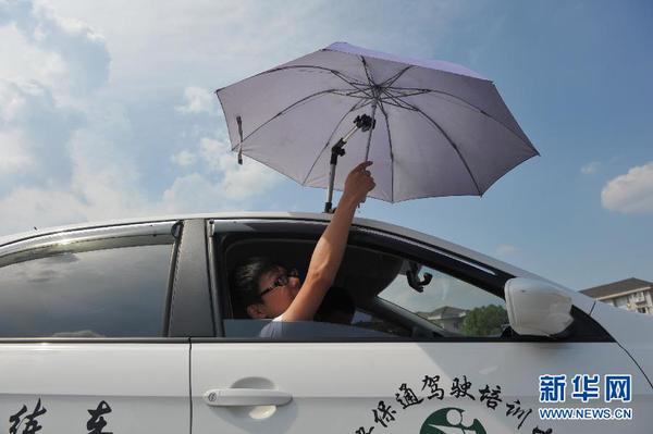 7月20日，在浙江省臨安市一家駕校內(nèi)，一名學(xué)員在車頂架著遮陽傘的教練車內(nèi)練習(xí)。