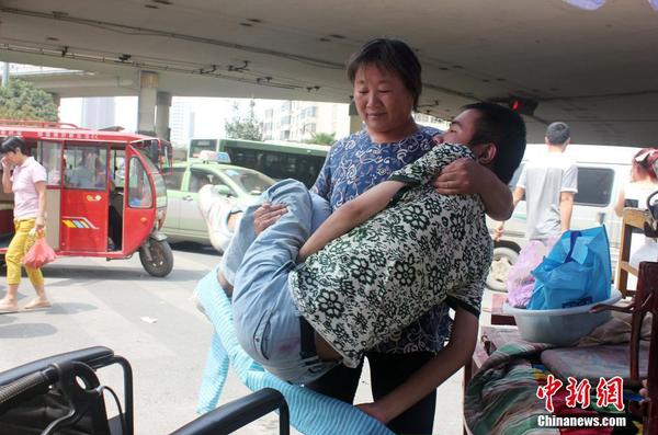 來到街頭“賣唱”點(diǎn)，呂愛梅熟練地把兒子把下三輪車，布置場(chǎng)地。 馬義恒 攝