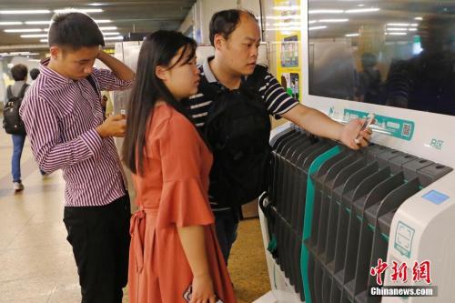 圖為沒帶雨傘的民眾在共享雨傘的貨架上掃碼借用。殷立勤 攝