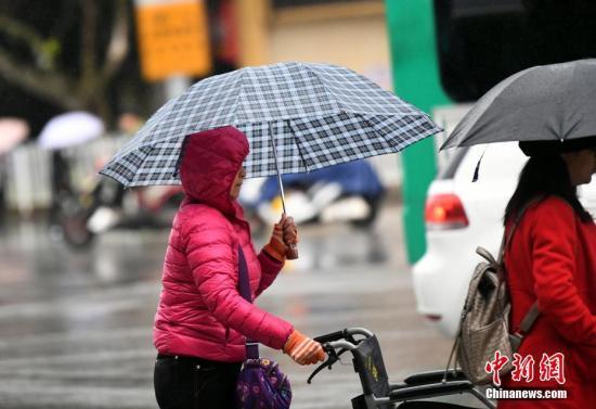 資料圖：昆明市區(qū)里身著羽絨服冒雨趕路的民眾。 中新社記者 李進紅 攝